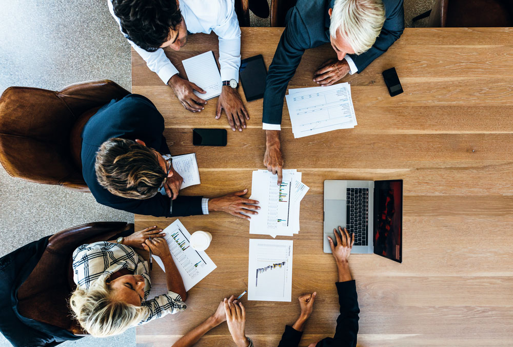 View from the top of four individuals sitting around a table looking at papers with graphs.