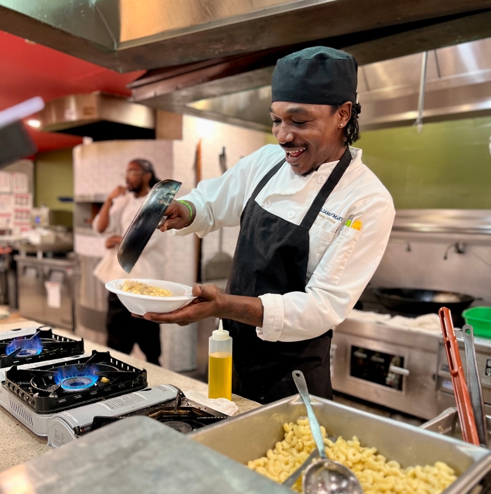 A W&M chef smiles while pouring pasta into a bowl.