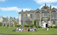 GotGothic-style historic two-story building on the campus of St Andrews in Scotland with students relaxing on green grass in the foreground